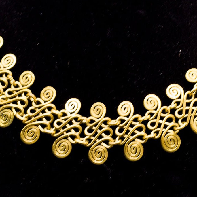 Quimbaya Necklace Close up. Intricate spiral pattern on top and bottom pieces creating a woven metal look. 